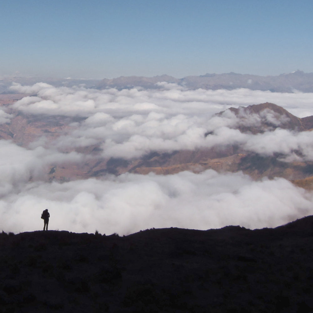 silhouette of a person hiking with a large rucksack above the clouds